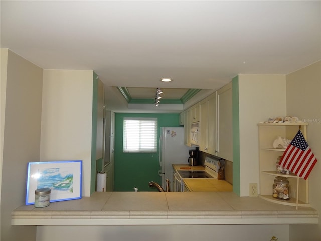 kitchen featuring tile countertops, white appliances, kitchen peninsula, and a tray ceiling