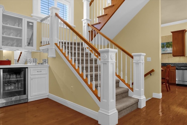 stairway with wine cooler, wood-type flooring, indoor bar, and ornamental molding