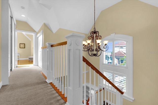 hall with an inviting chandelier, light colored carpet, and vaulted ceiling