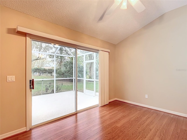 empty room with a textured ceiling, light hardwood / wood-style flooring, and vaulted ceiling