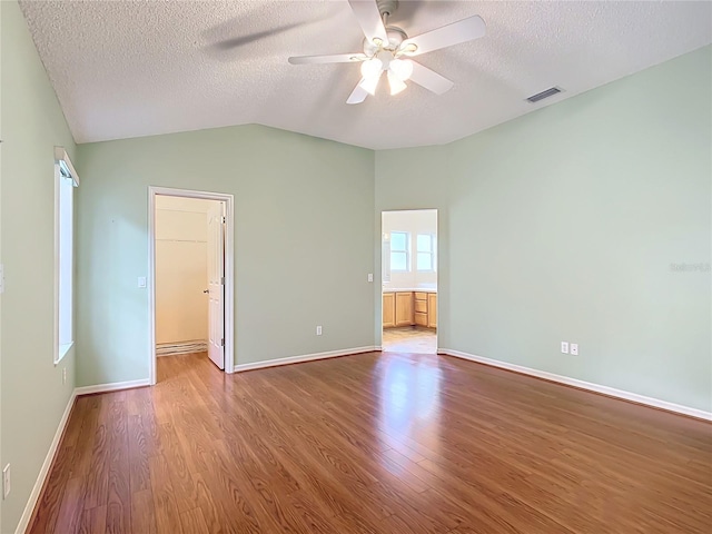 empty room with a textured ceiling, hardwood / wood-style flooring, vaulted ceiling, and ceiling fan