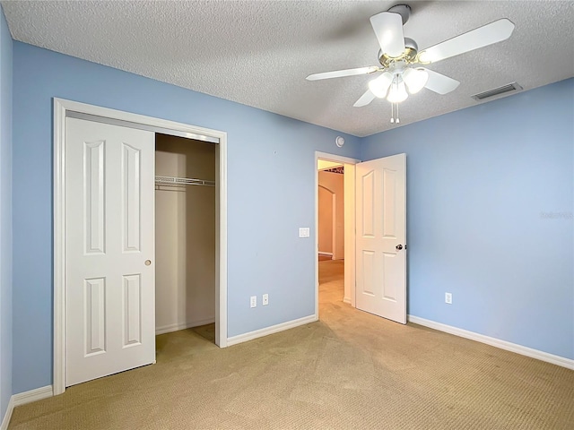 unfurnished bedroom with ceiling fan, a closet, light colored carpet, and a textured ceiling