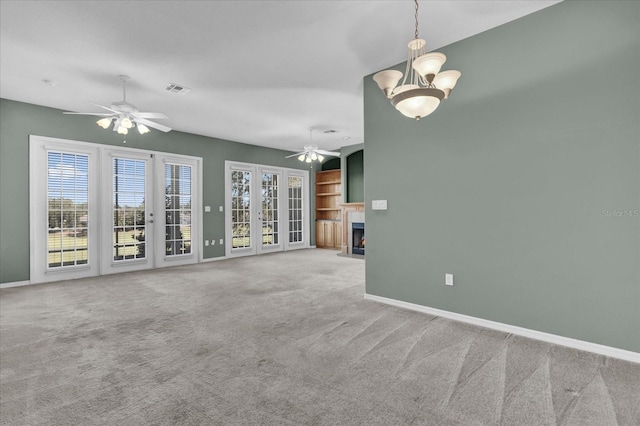 unfurnished living room featuring carpet flooring, ceiling fan with notable chandelier, and a healthy amount of sunlight