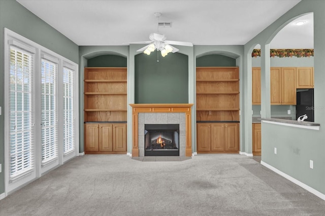 unfurnished living room featuring light carpet, a fireplace, ceiling fan, and built in features