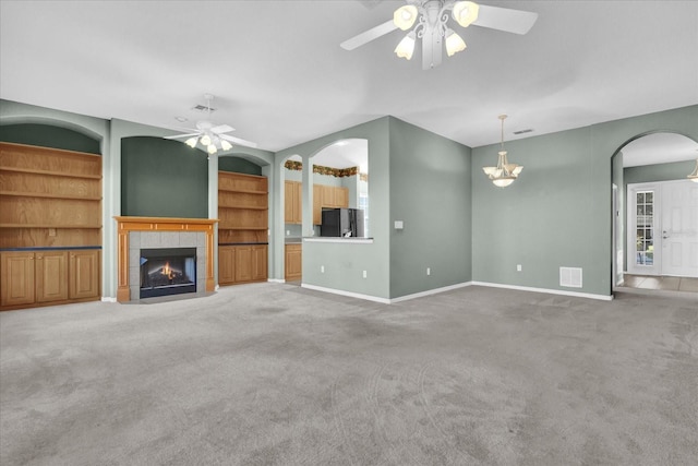 unfurnished living room featuring built in shelves, ceiling fan, a fireplace, and carpet floors