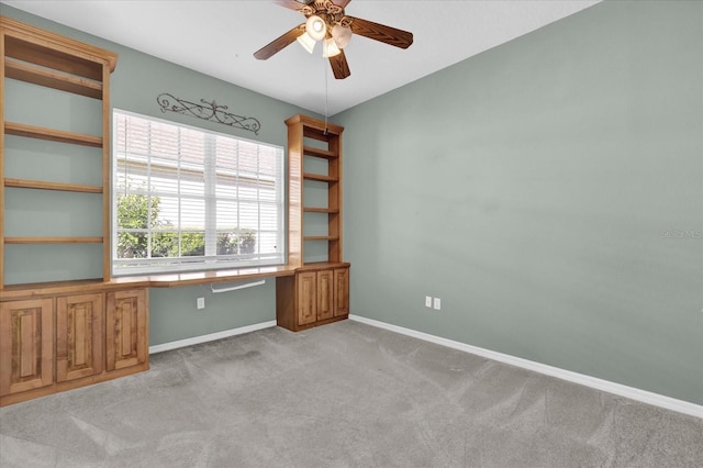 carpeted empty room featuring ceiling fan and built in desk