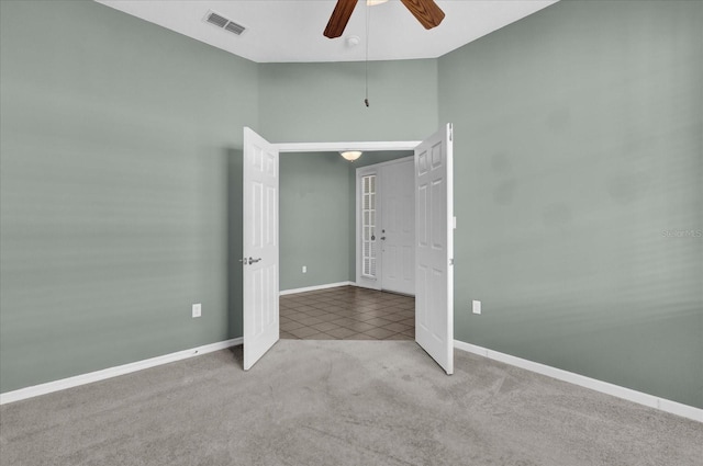 carpeted empty room featuring ceiling fan and a towering ceiling