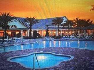 pool at dusk with a patio and a hot tub