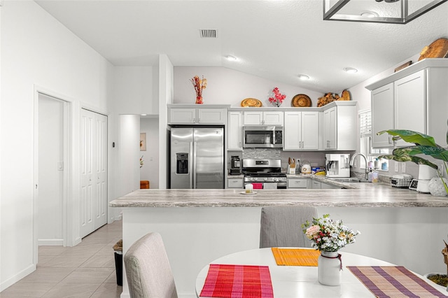 kitchen with lofted ceiling, sink, light tile patterned floors, appliances with stainless steel finishes, and kitchen peninsula