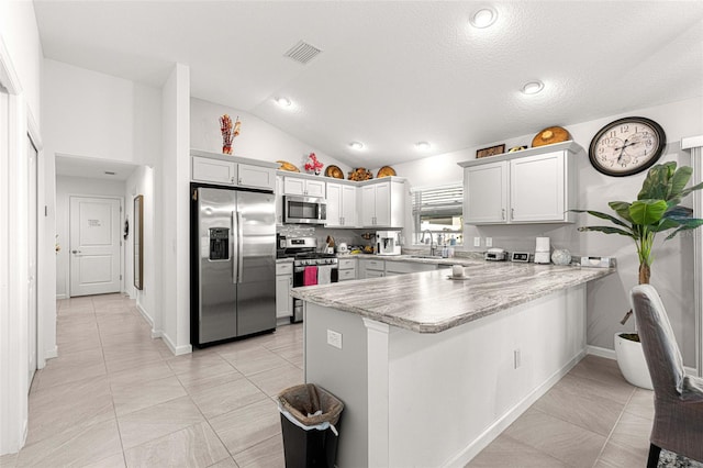 kitchen with kitchen peninsula, appliances with stainless steel finishes, vaulted ceiling, light tile patterned floors, and white cabinetry