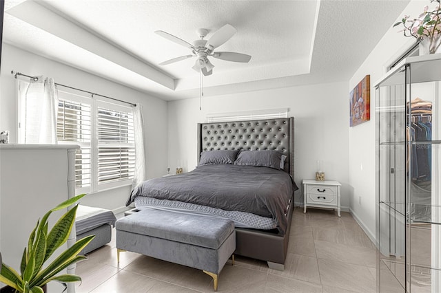 bedroom with a textured ceiling, a raised ceiling, ceiling fan, light tile patterned floors, and a closet