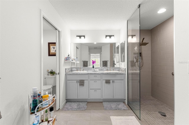 bathroom with vanity, a textured ceiling, tiled shower, and tile patterned floors