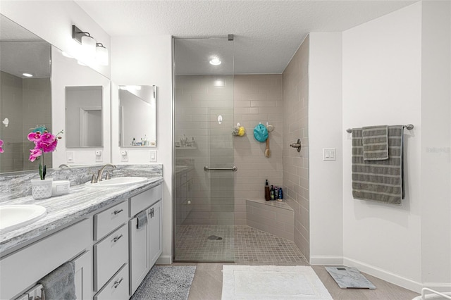 bathroom with tile patterned floors, vanity, a tile shower, and a textured ceiling