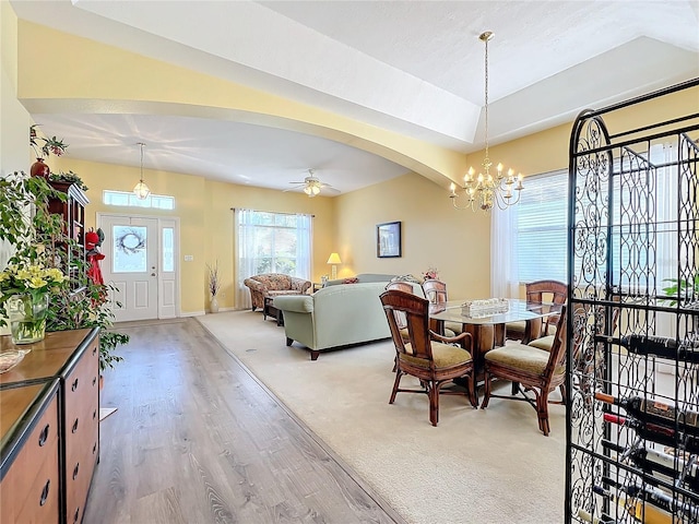 dining space with a raised ceiling, ceiling fan with notable chandelier, and light hardwood / wood-style floors