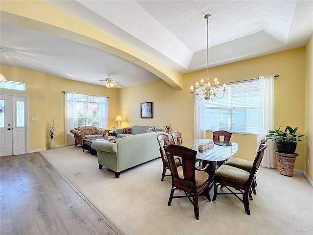 dining area with ceiling fan with notable chandelier, light colored carpet, and a raised ceiling