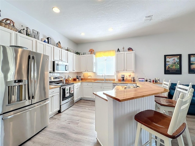 kitchen with a breakfast bar, butcher block counters, sink, white cabinetry, and stainless steel appliances