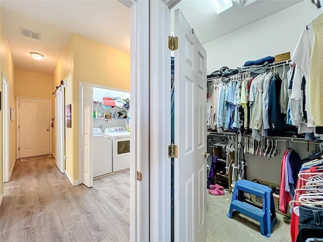 spacious closet with washer and clothes dryer and light hardwood / wood-style flooring