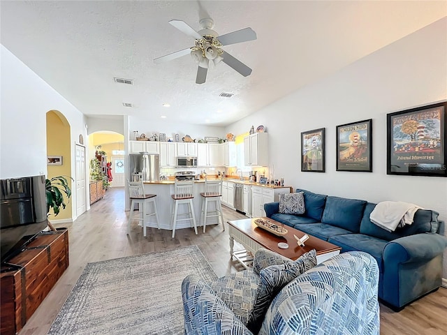 living room featuring ceiling fan, light hardwood / wood-style flooring, sink, and a textured ceiling