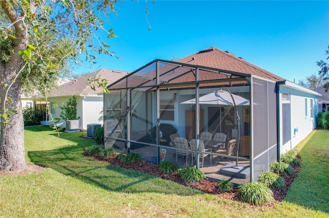 rear view of house featuring a patio, a yard, central AC, and glass enclosure