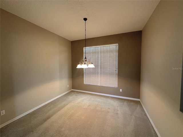 empty room featuring carpet, a textured ceiling, and an inviting chandelier