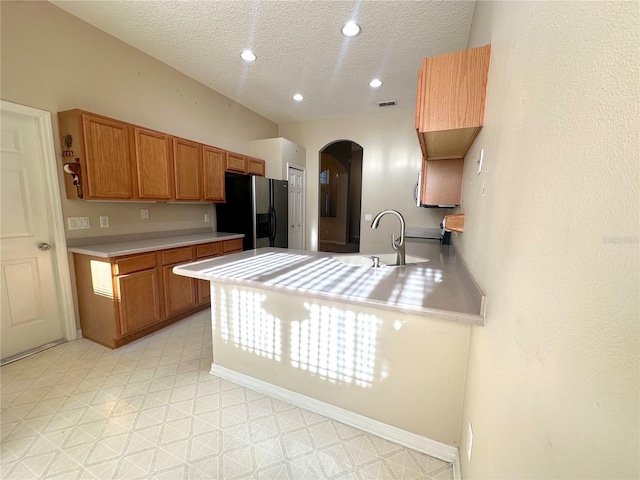 kitchen with kitchen peninsula, stainless steel fridge with ice dispenser, sink, and a textured ceiling