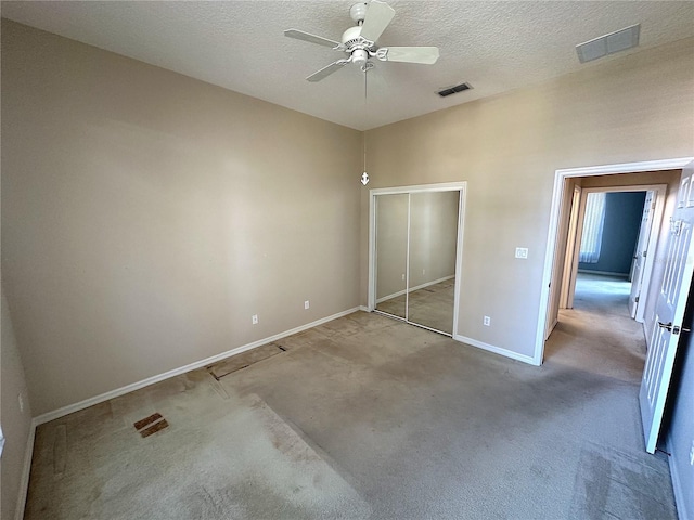 unfurnished bedroom featuring ceiling fan, a closet, light carpet, and a textured ceiling