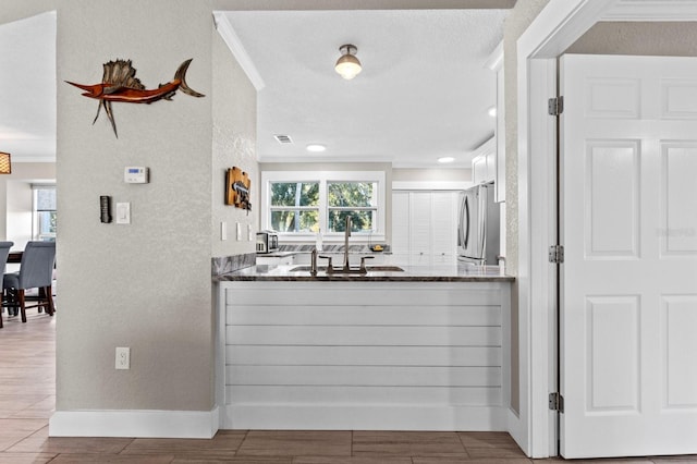 kitchen featuring stainless steel fridge, ornamental molding, dark stone counters, and sink