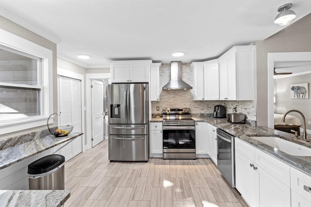 kitchen with appliances with stainless steel finishes, wall chimney exhaust hood, sink, stone countertops, and white cabinets