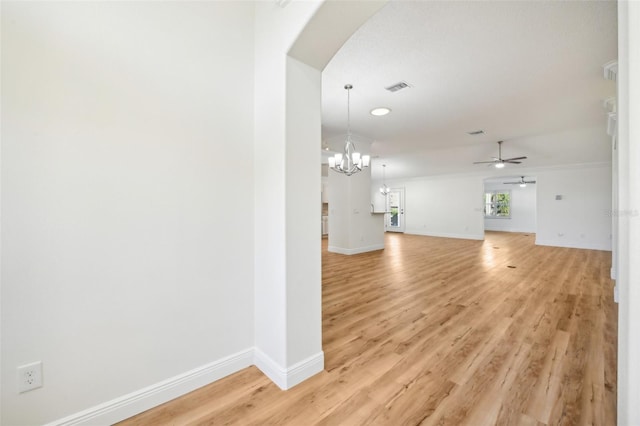 unfurnished living room with ceiling fan with notable chandelier, light hardwood / wood-style flooring, and crown molding