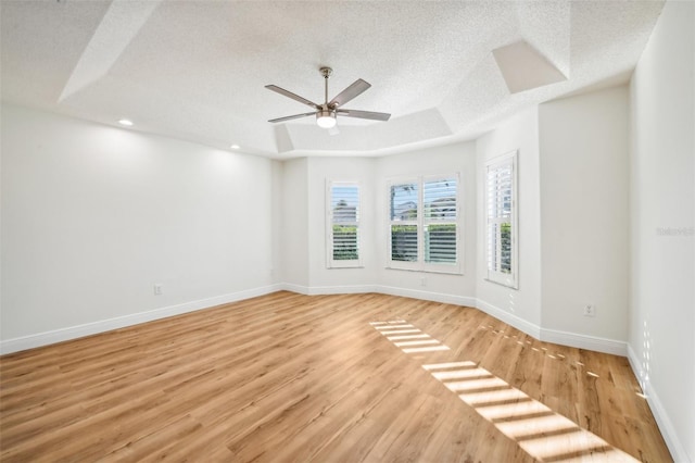 spare room with a raised ceiling, ceiling fan, a textured ceiling, and light wood-type flooring