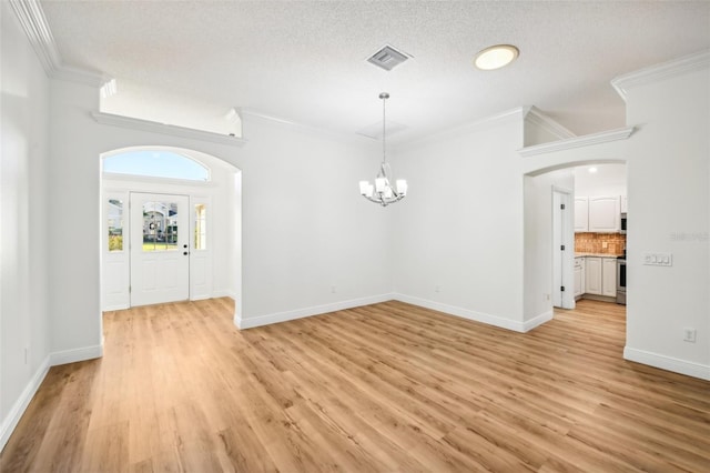 spare room featuring a chandelier, a textured ceiling, light hardwood / wood-style flooring, and crown molding