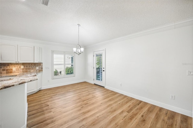 unfurnished dining area with a textured ceiling, an inviting chandelier, light hardwood / wood-style flooring, and ornamental molding