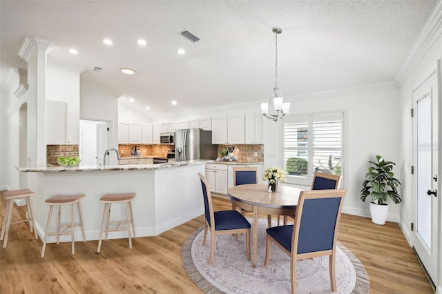 dining space featuring ornamental molding, a textured ceiling, sink, light hardwood / wood-style flooring, and a notable chandelier