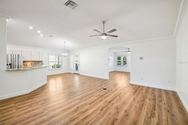 unfurnished living room featuring ceiling fan with notable chandelier, ornamental molding, a wealth of natural light, and light hardwood / wood-style flooring