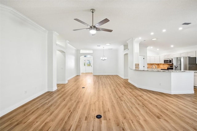 unfurnished living room featuring ceiling fan with notable chandelier, sink, crown molding, light wood-type flooring, and a textured ceiling