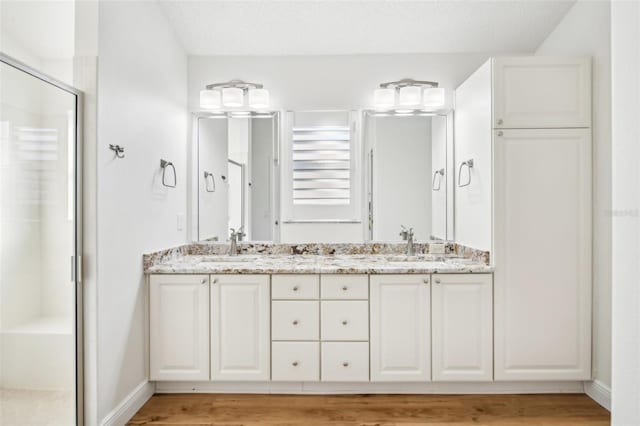 bathroom with a textured ceiling, vanity, hardwood / wood-style flooring, and a shower with door