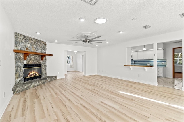 unfurnished living room with a fireplace, a textured ceiling, light wood-type flooring, and ceiling fan