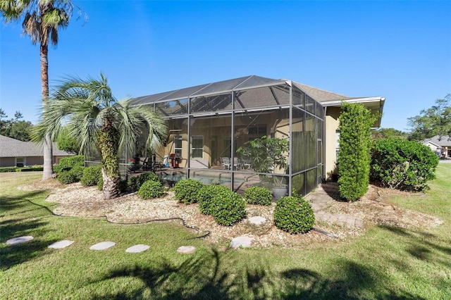 rear view of house with a pool, a yard, and glass enclosure