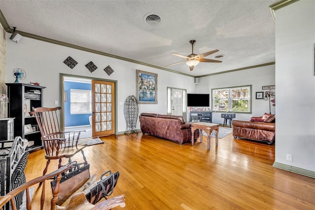 living room featuring wood-type flooring, a textured ceiling, ceiling fan, and ornamental molding