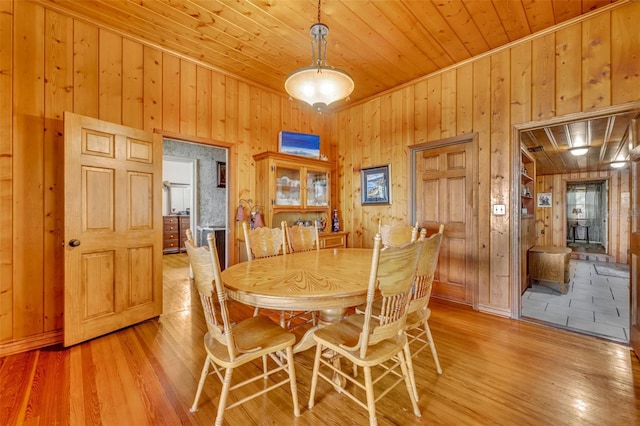 dining area with light wood-type flooring, wood ceiling, crown molding, and wood walls