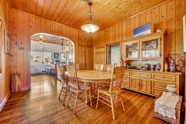 dining space with ceiling fan, light wood-type flooring, wooden walls, and wooden ceiling