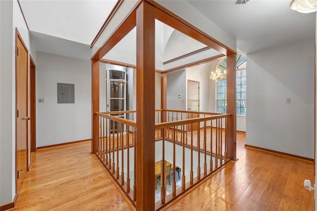 corridor with electric panel, light hardwood / wood-style floors, and a notable chandelier