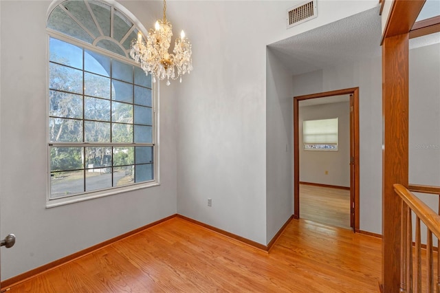 spare room with a textured ceiling, light hardwood / wood-style flooring, a wealth of natural light, and a notable chandelier