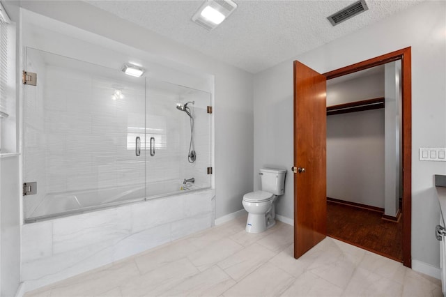 bathroom featuring bath / shower combo with glass door, a textured ceiling, and toilet