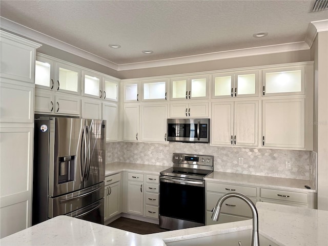 kitchen with light stone counters, backsplash, appliances with stainless steel finishes, white cabinets, and ornamental molding