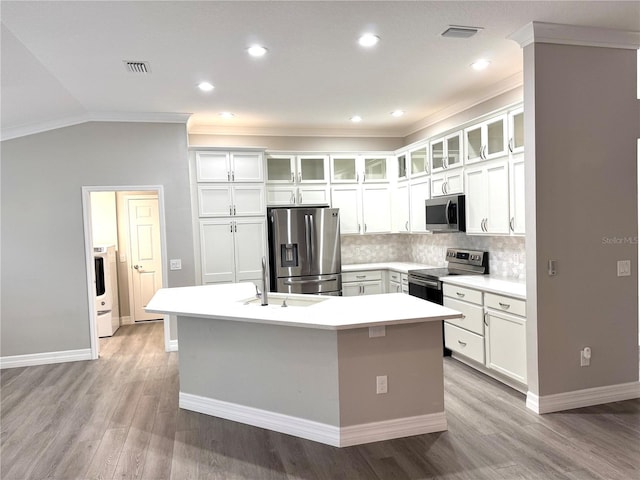 kitchen with appliances with stainless steel finishes, vaulted ceiling, light hardwood / wood-style flooring, and an island with sink