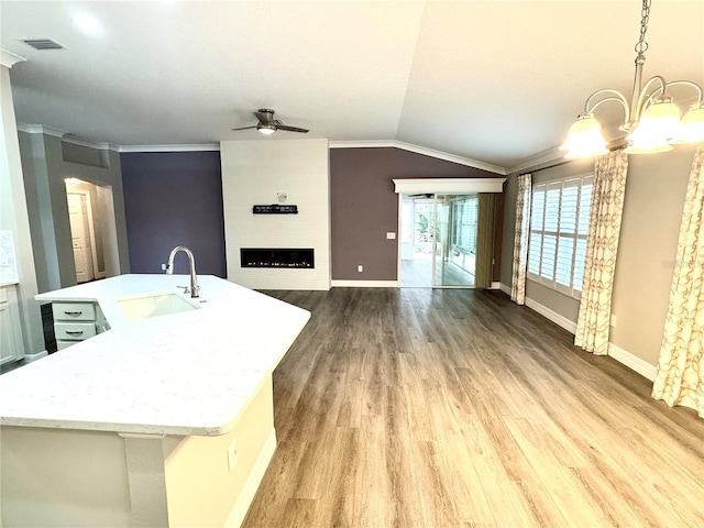 kitchen with light wood-type flooring, vaulted ceiling, sink, pendant lighting, and a center island with sink