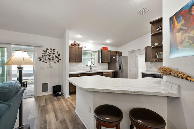 kitchen with kitchen peninsula, stainless steel refrigerator with ice dispenser, a breakfast bar, sink, and light hardwood / wood-style floors