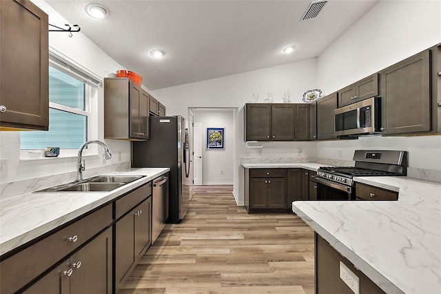 kitchen with appliances with stainless steel finishes, light hardwood / wood-style flooring, lofted ceiling, and sink