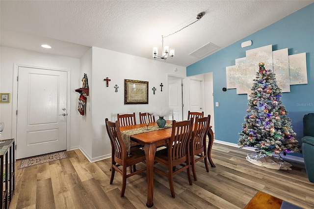 dining room featuring a textured ceiling, hardwood / wood-style flooring, vaulted ceiling, and a notable chandelier